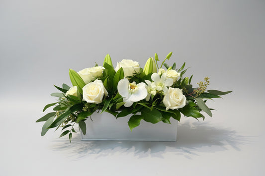 Floral arrangement with white flowers and green leaves in a tin container.
